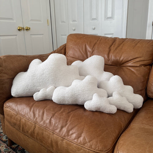 White cloud-shaped pillows on a brown leather couch in a room with gray walls and doors.