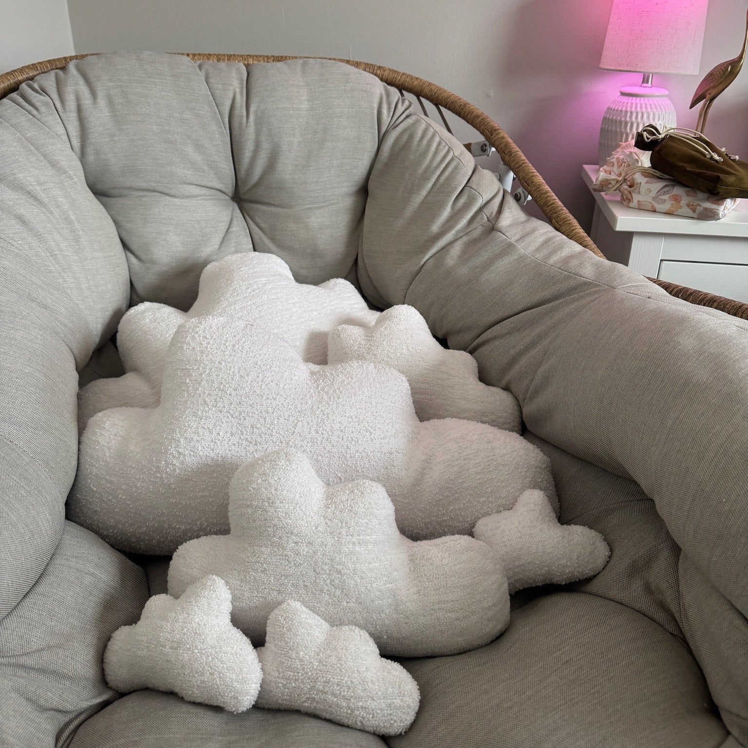 Cloud-shaped cushions on a round cushioned chair with a pink lamp in the background.