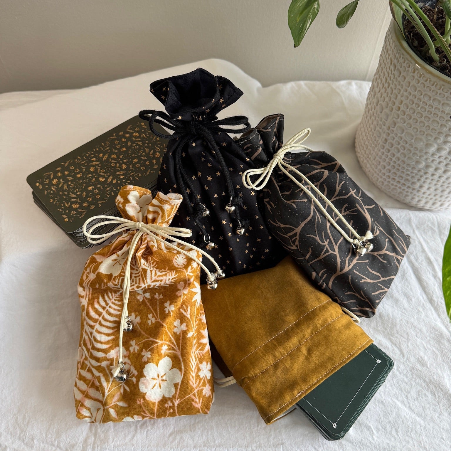Collection of dark colored drawstring bags and tarot decks on a white surface with a plant in the background