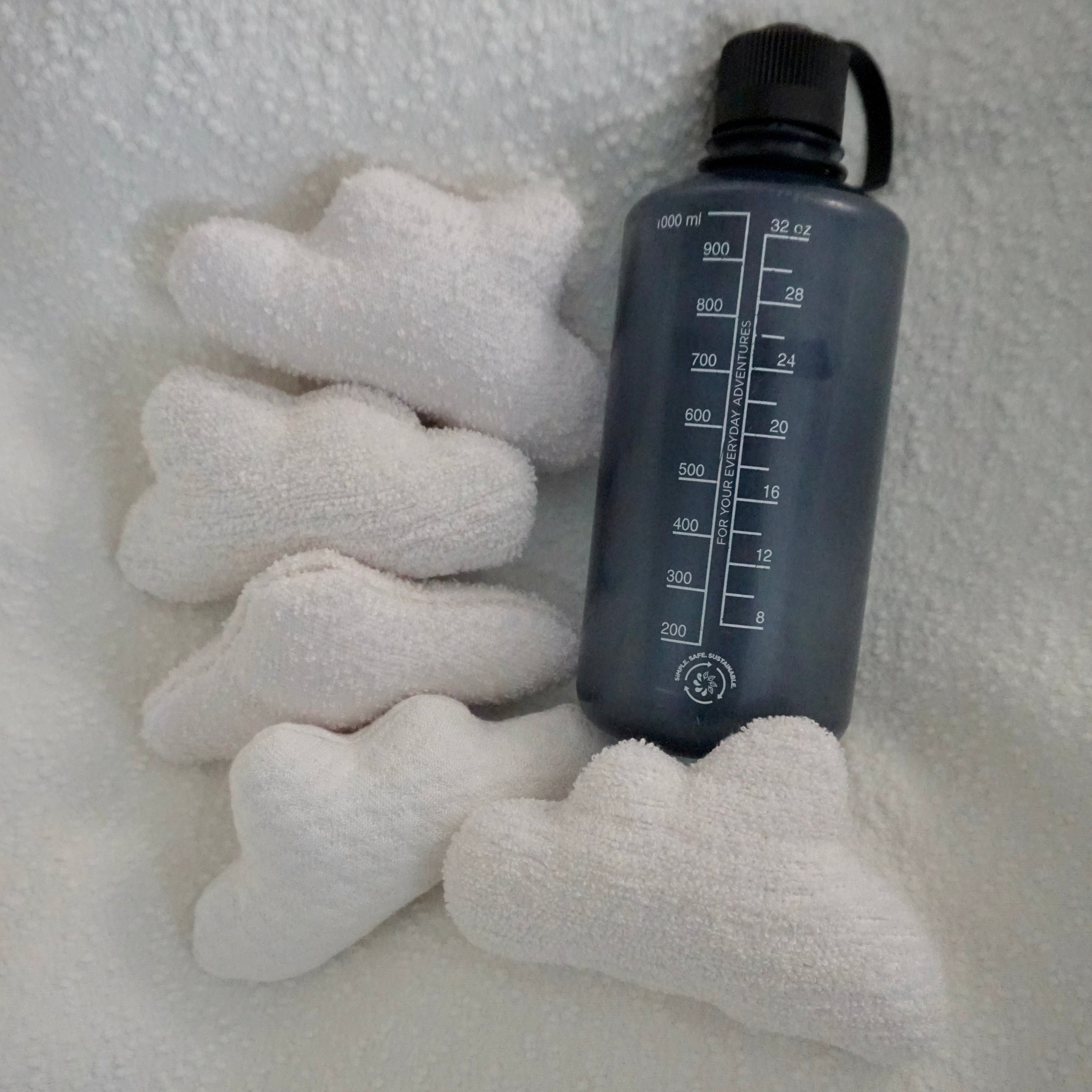Five extra small Cloud Pillows arranged together on a textured white blanket with a water bottle for scale.