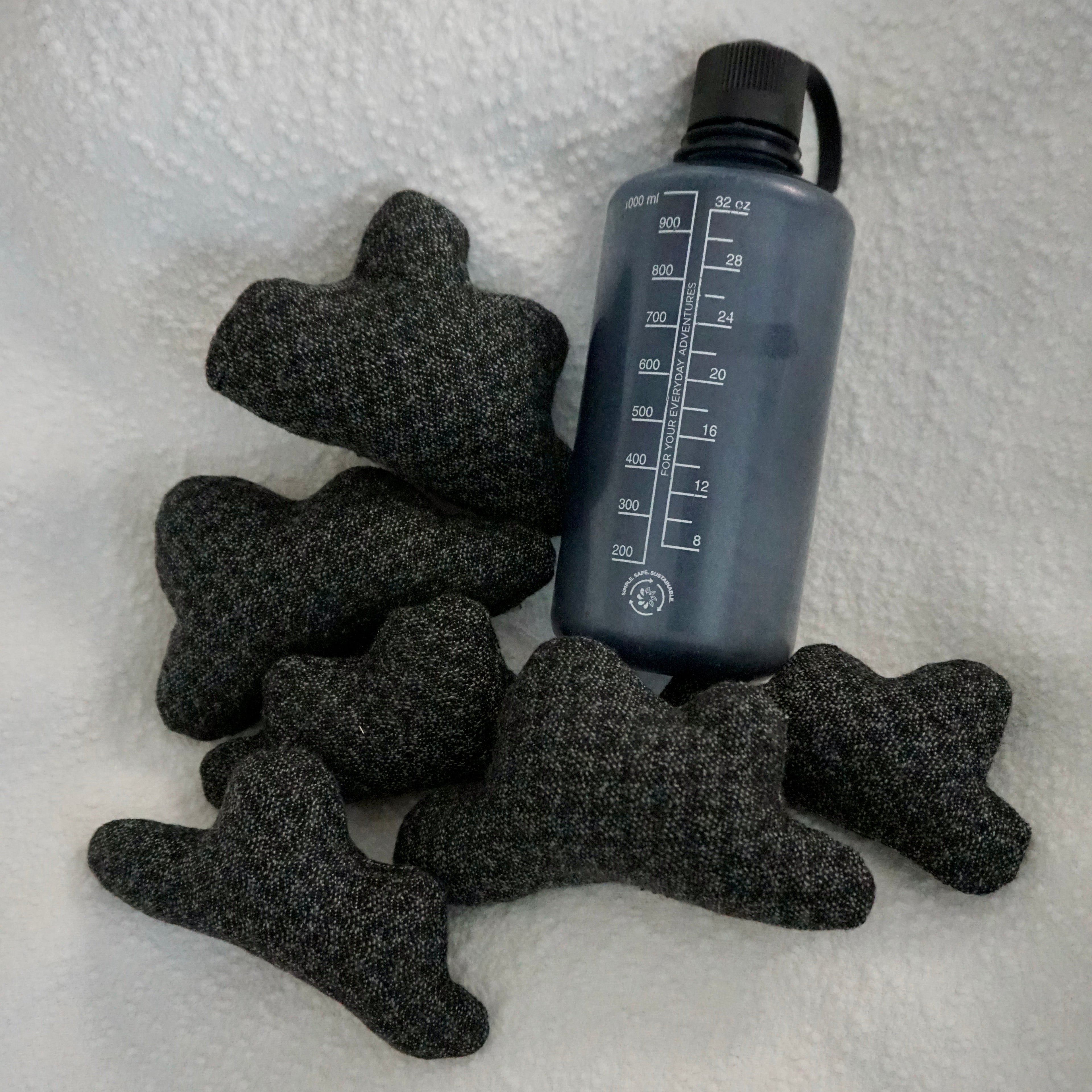 Six extra small Storm Cloud Pillows on a textured white blanket with water bottle for scale.