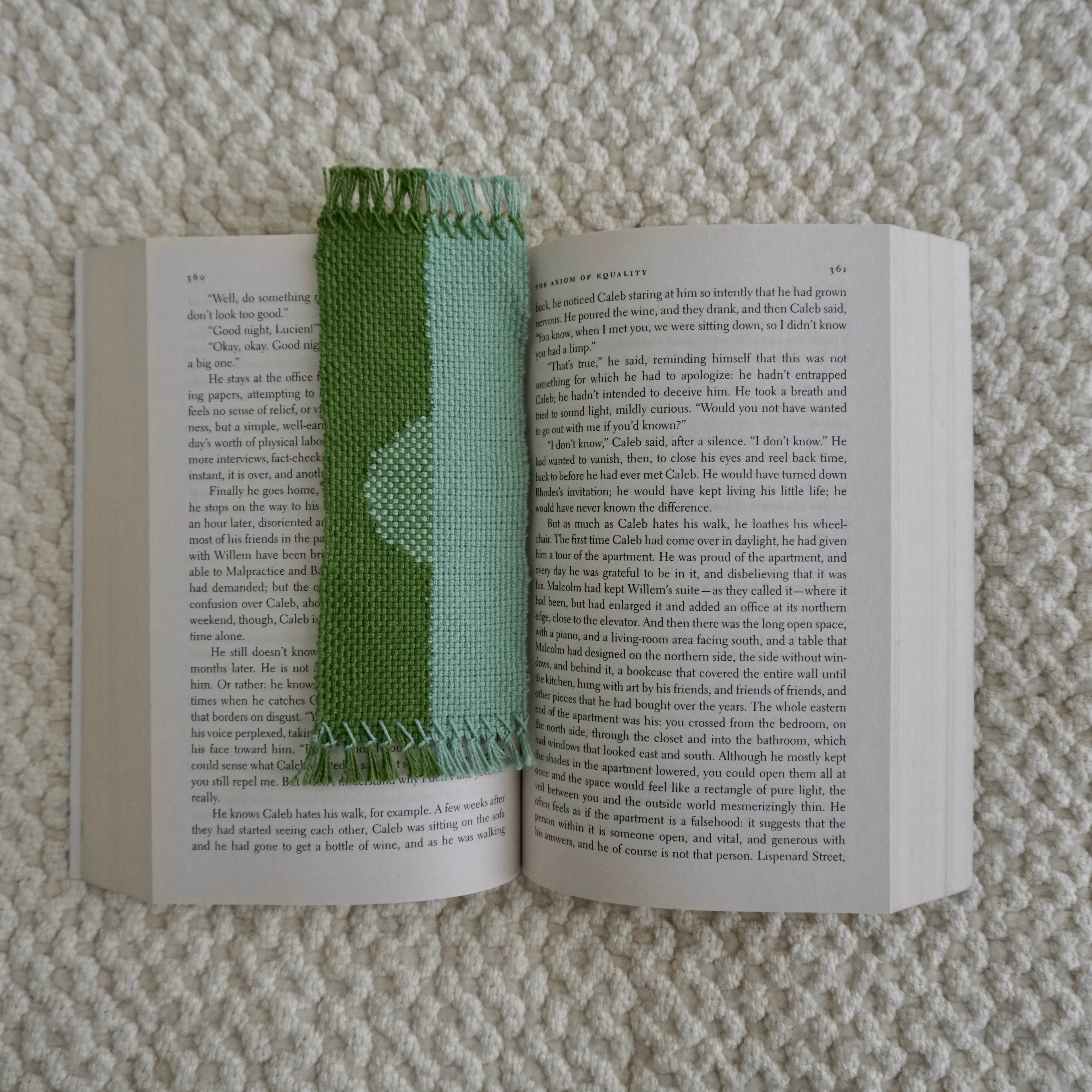 A blue and green bookmark with a half moon design in an open book on a beige textured blanket.