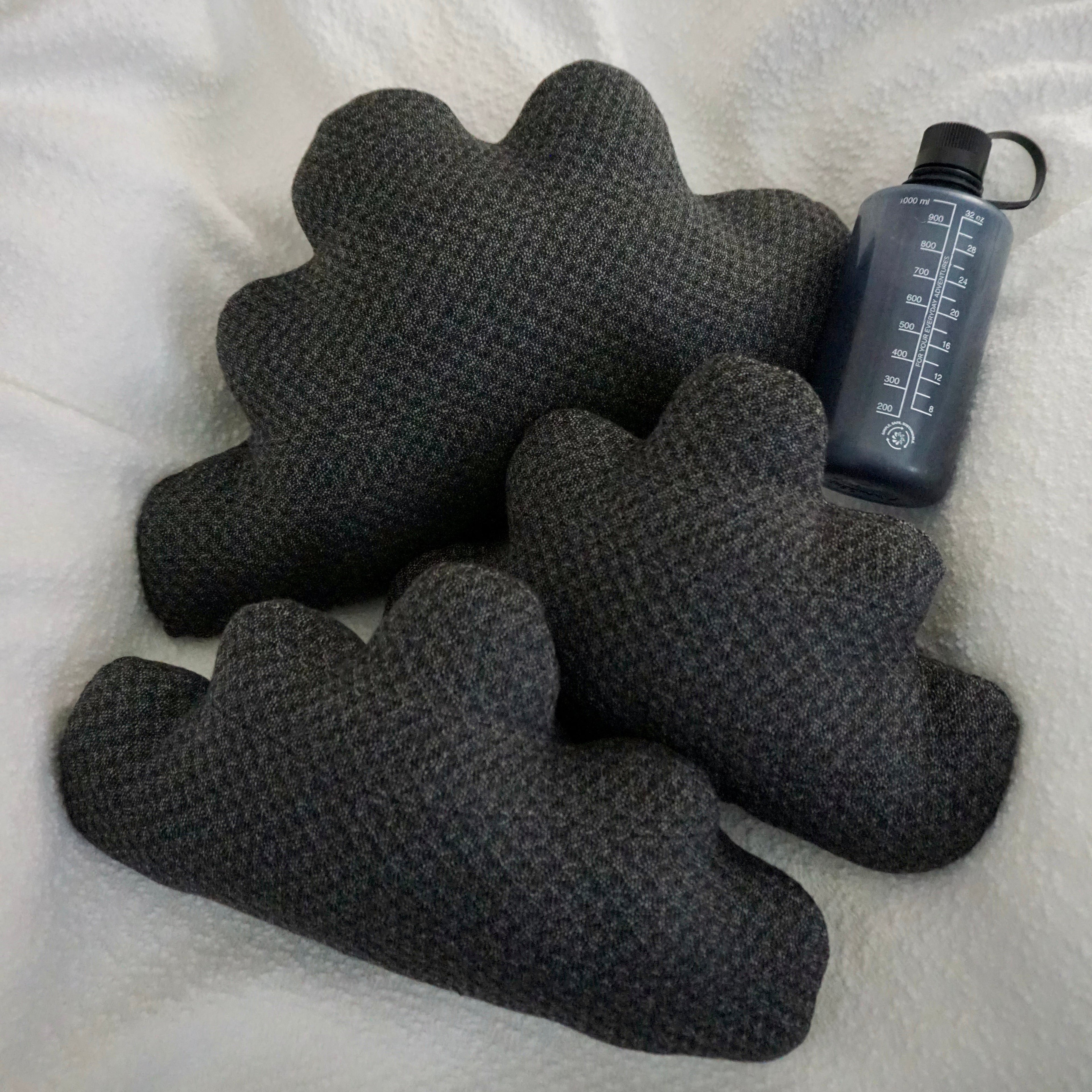 Three large Storm Cloud Pillows arranged on a textured white blanket with a water bottle for scale.