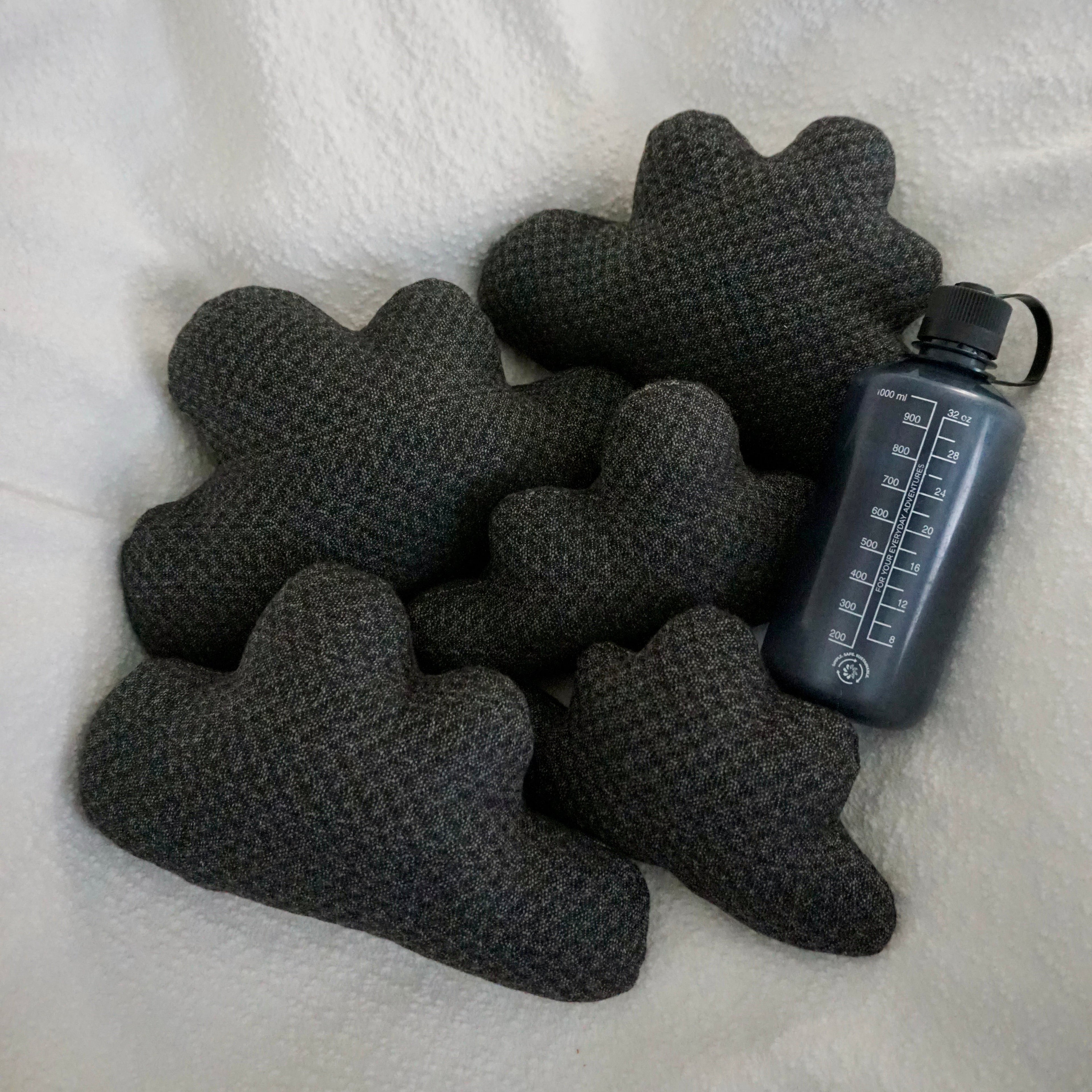 Five medium Storm Cloud Pillows arranged on a textured white blanket with water bottle for scale.