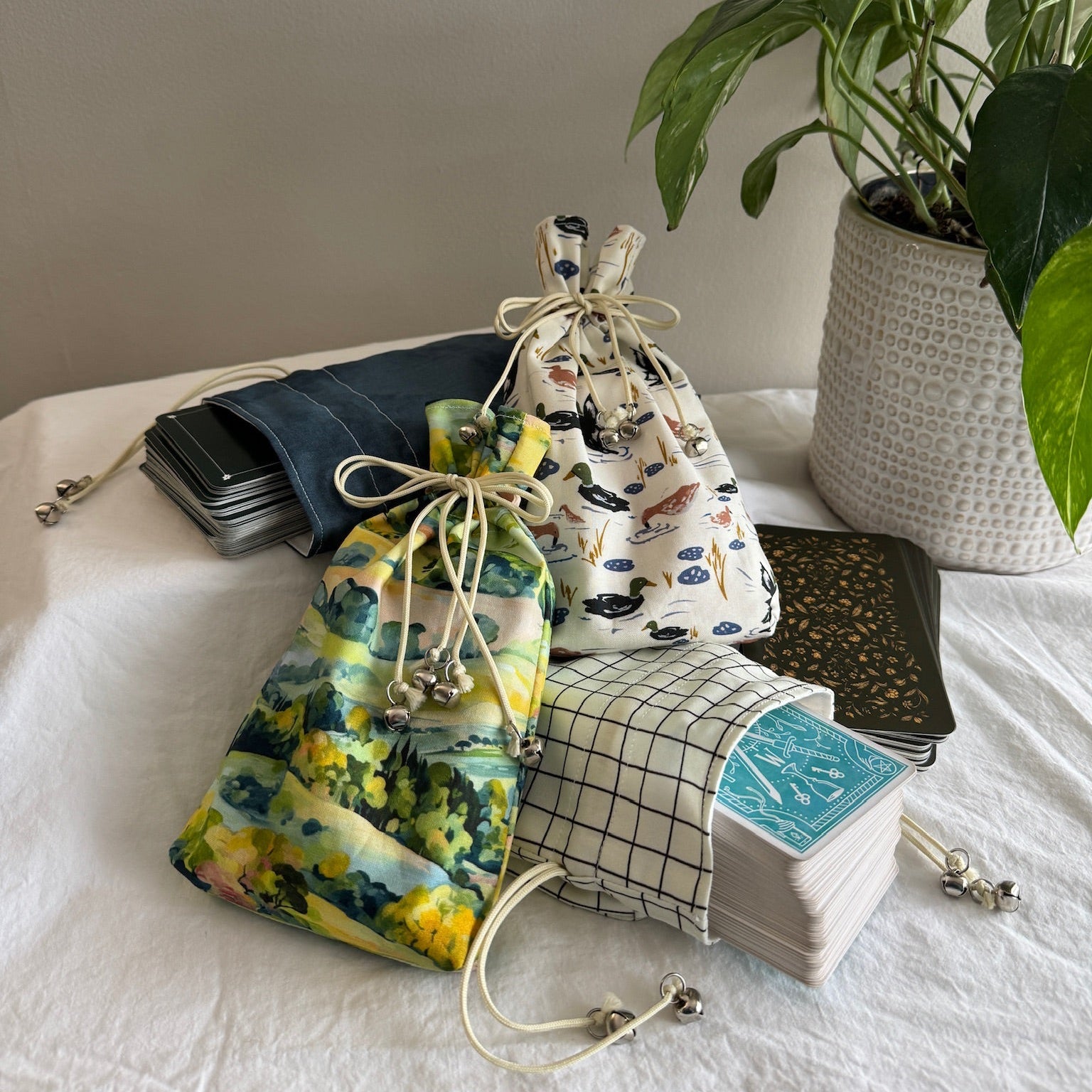 Four drawstring bags with different patterns on a white surface with a plant and tarot decks in the background.
