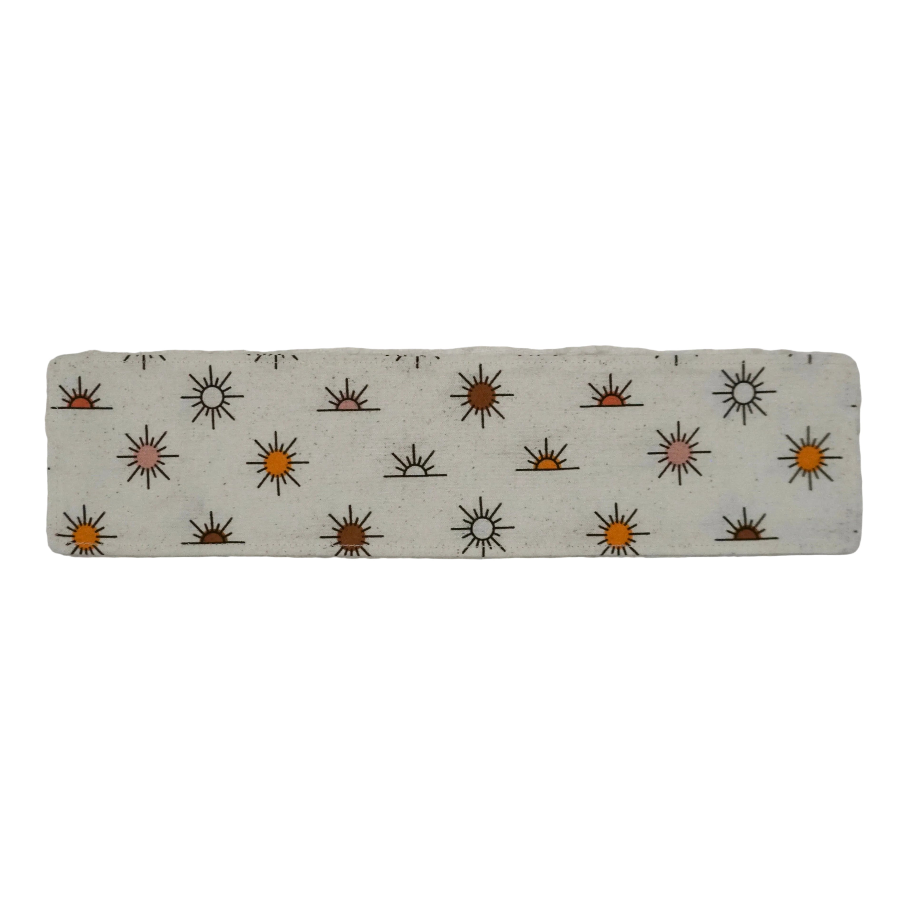 Off-white fabric bookmark with warm-toned sun pattern on a white background