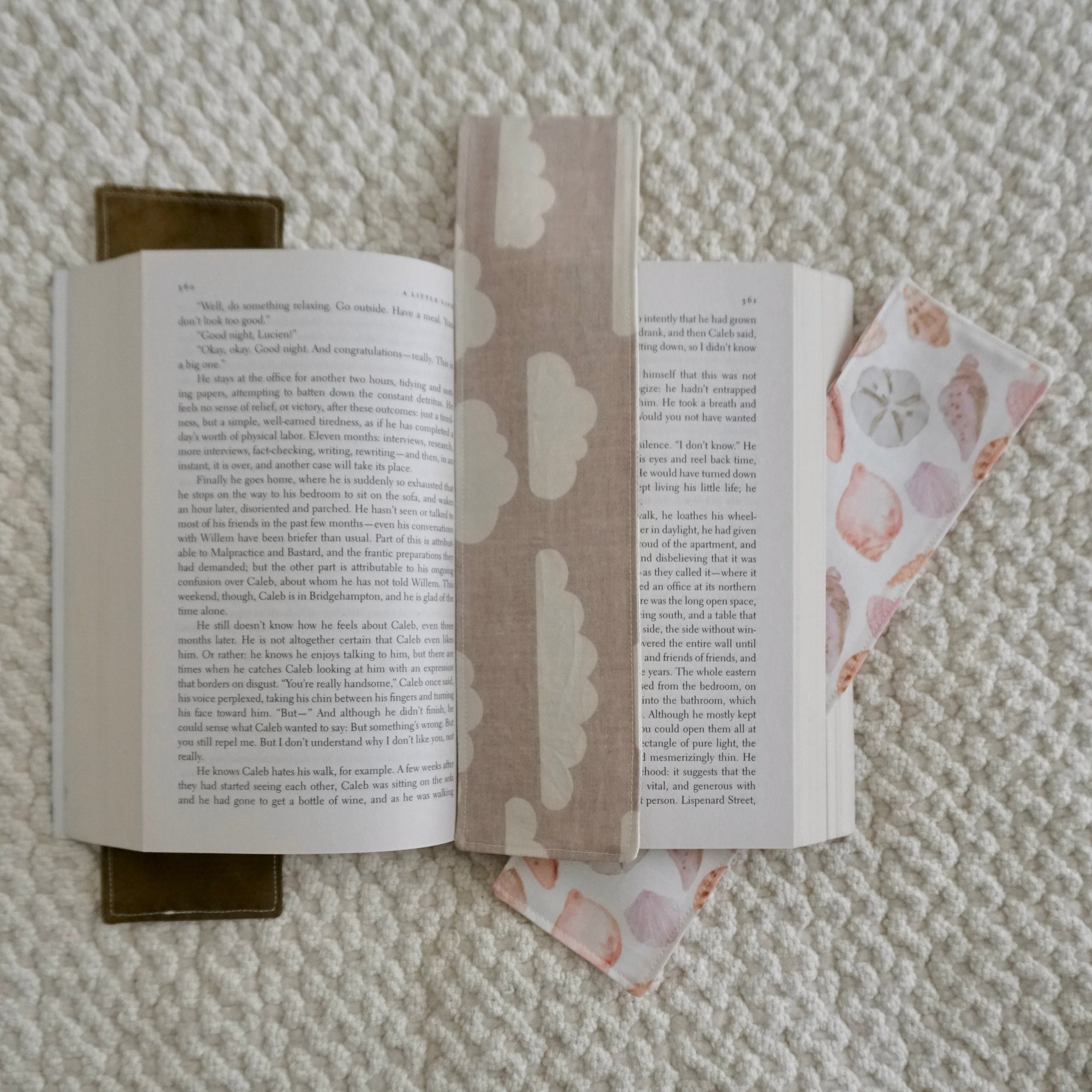 Three beige toned bookmarks inside an open book on a textured blanket.