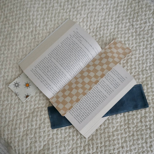 Three bookmarks arranged in an open book resting on a beige textured blanket.