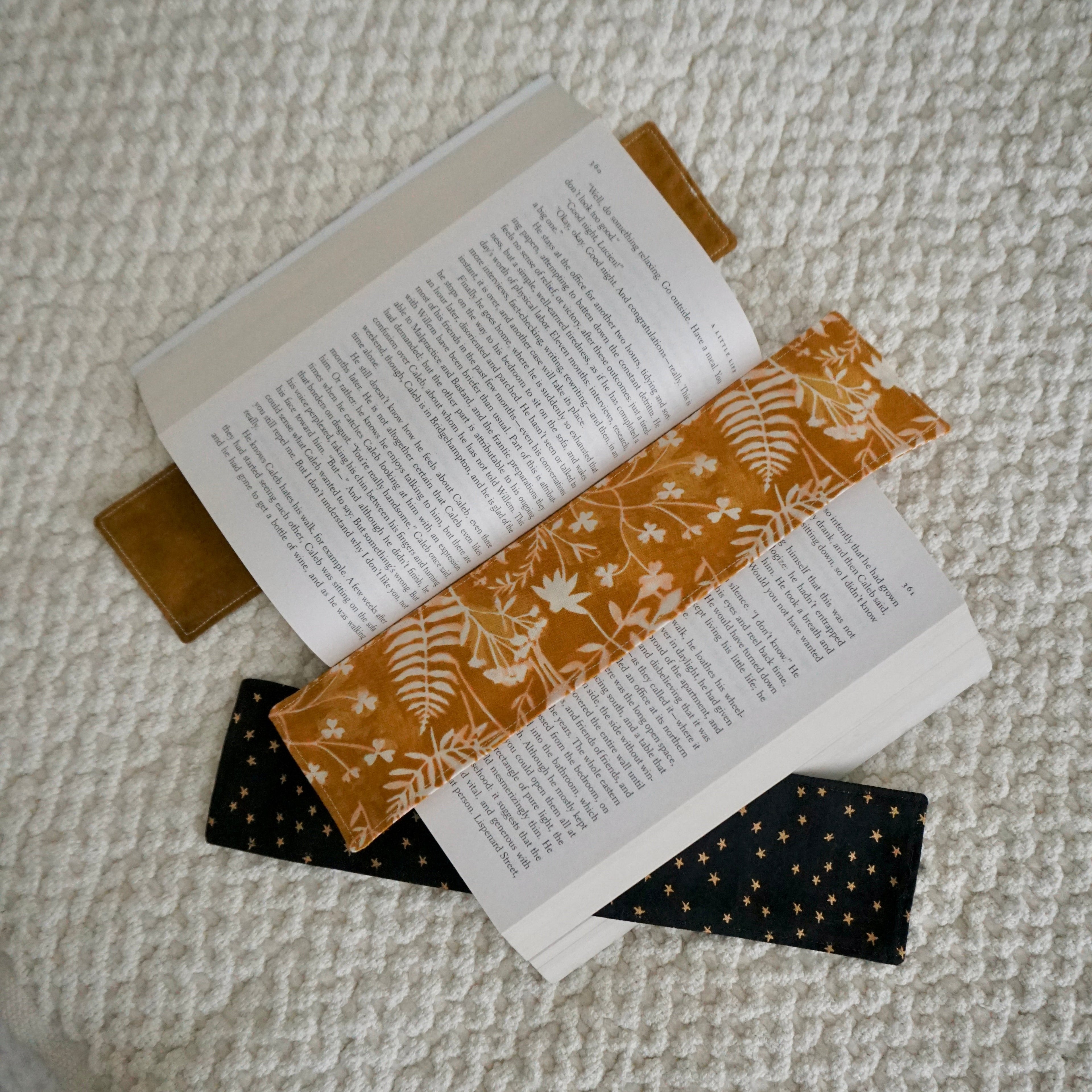 Three warm-toned bookmarks in an open book on a textured beige blanket.