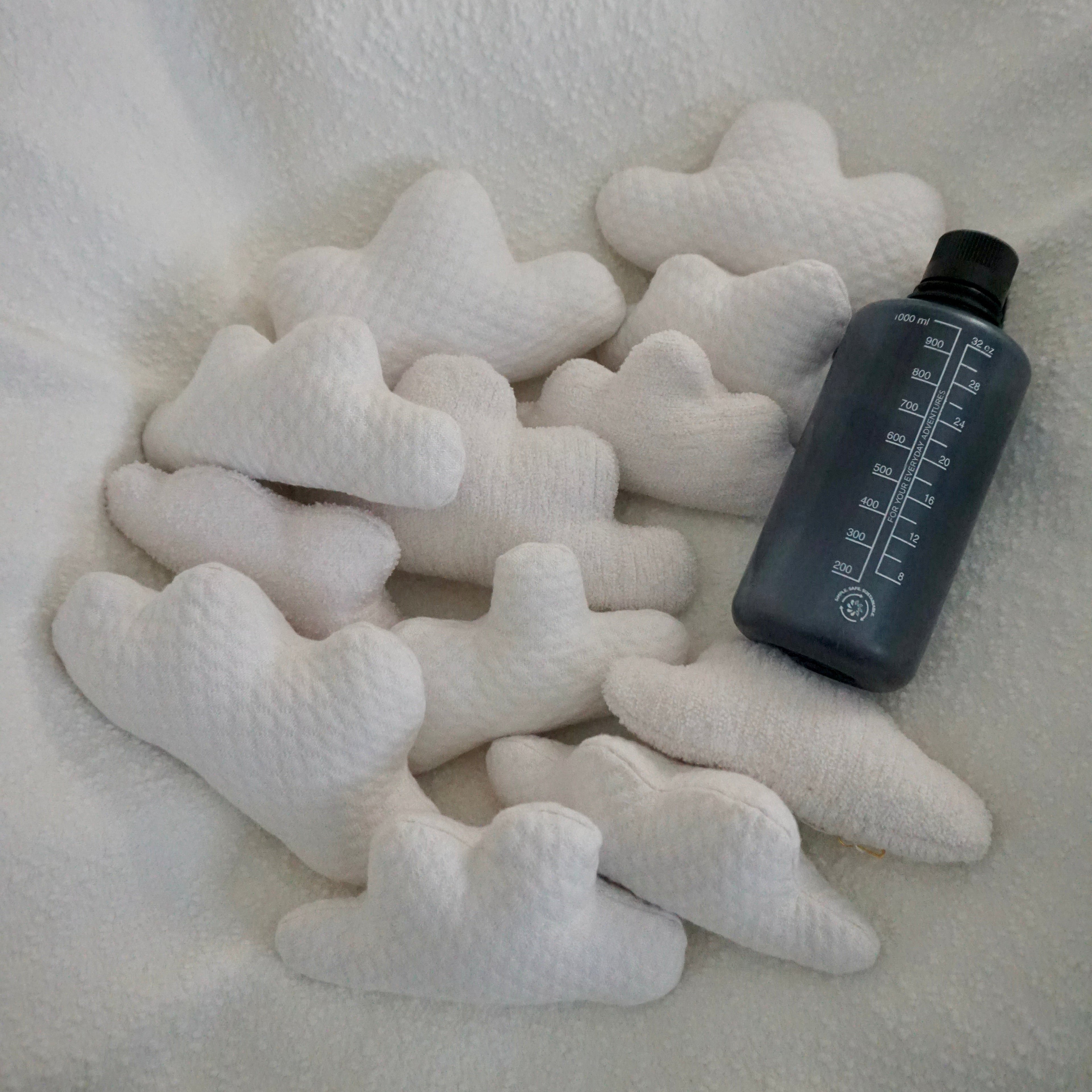 Twelve small Cloud Pillows arranged together on a textured white blanket with a water bottle for scale.