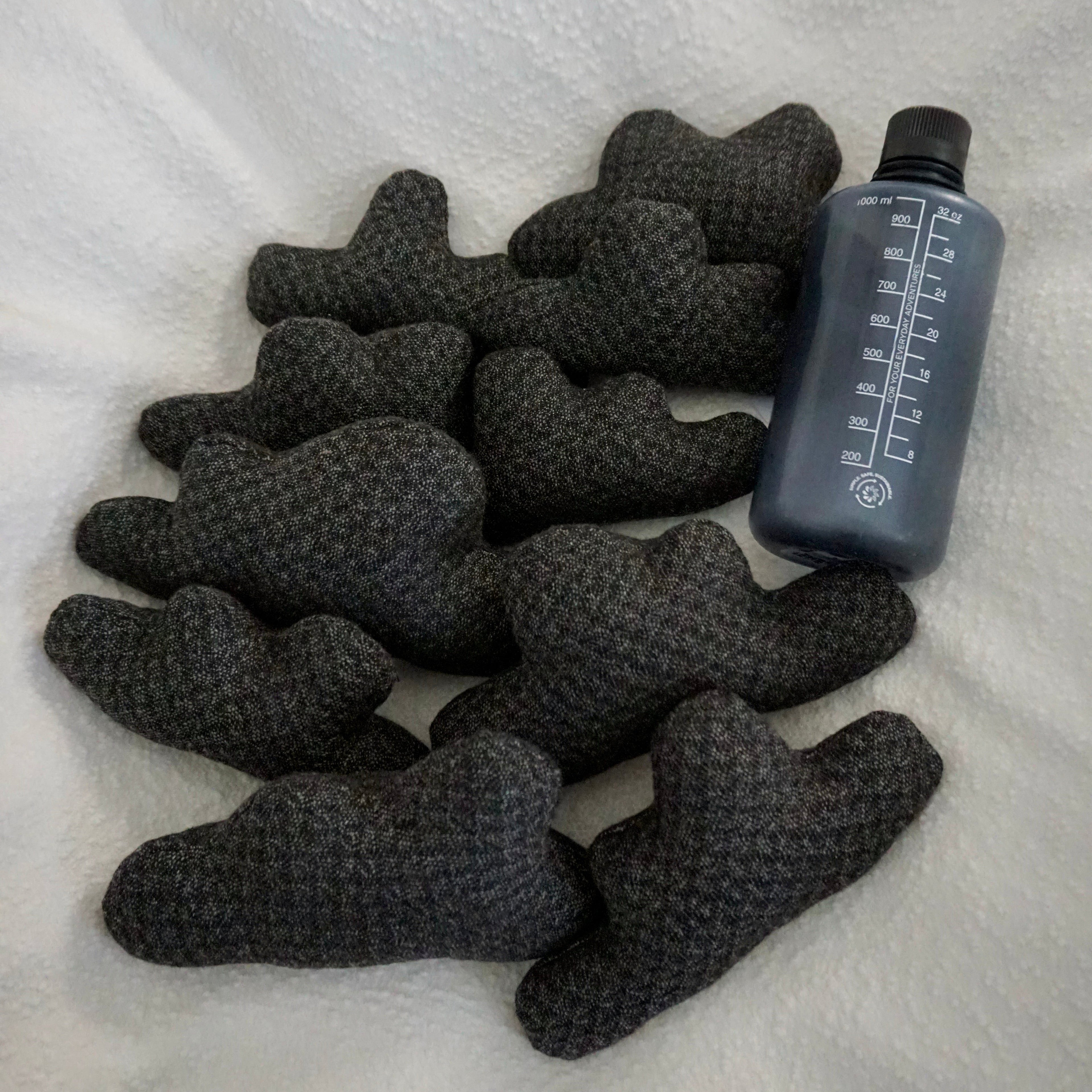 Ten small Storm Cloud Pillows on a textured white blanket with water bottle for scale.
