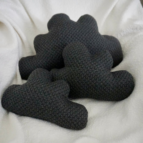 Three storm cloud pillows made from dark gray quilted fabric in a chair with a white boucle blanket thrown over it.