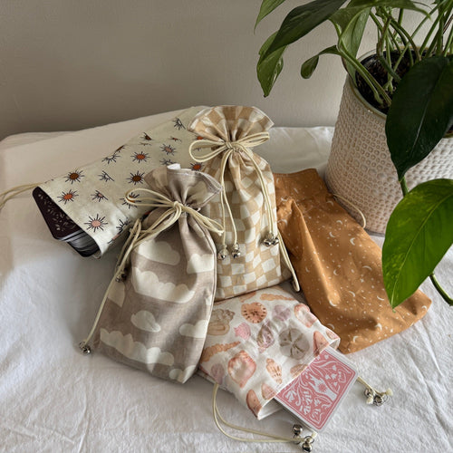 Set of warm-toned drawstring bags on a white surface with a plant and tarot decks in the background