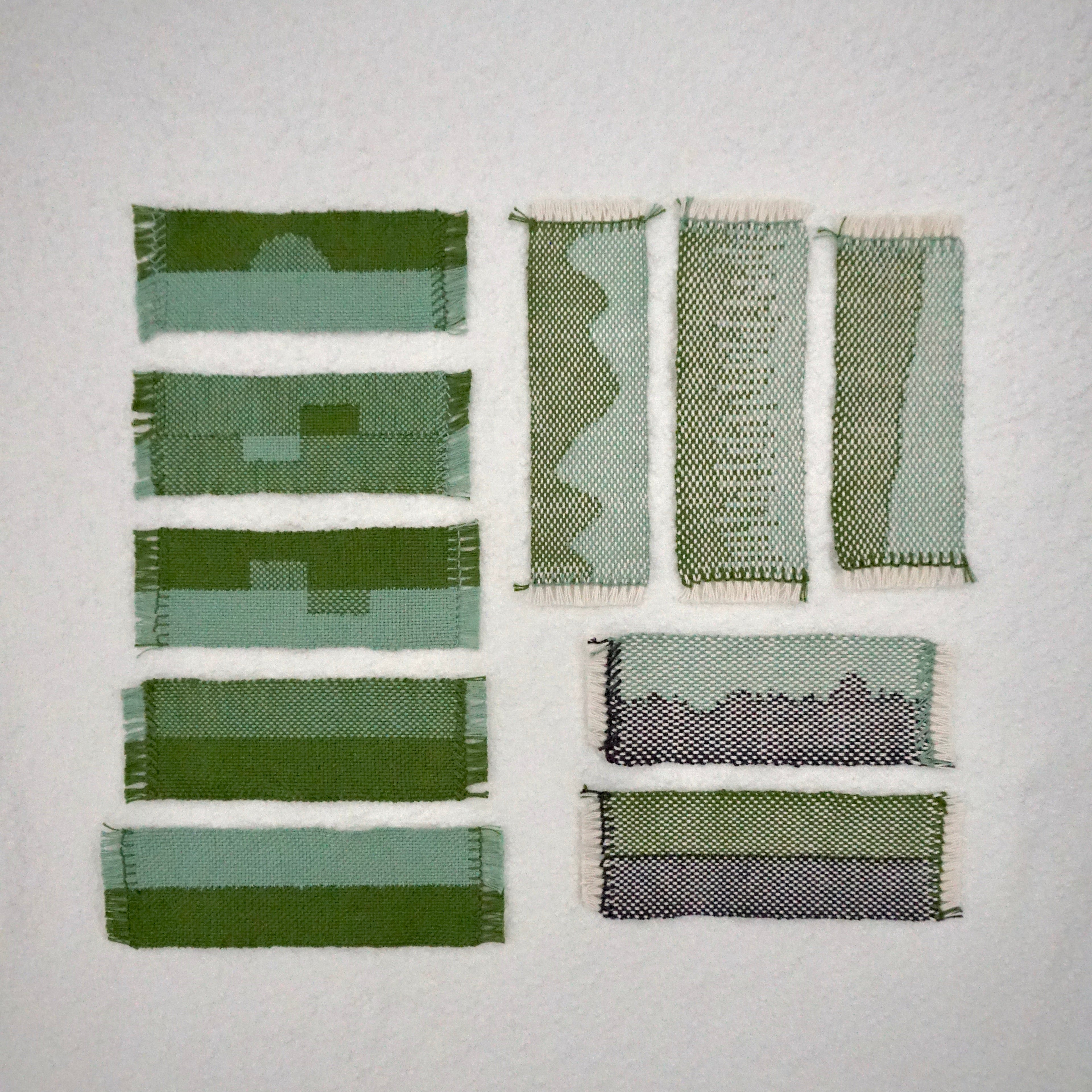 Ten woven bookmarks in patterns of green, blue, gray, and white laid out together on a textured white background.